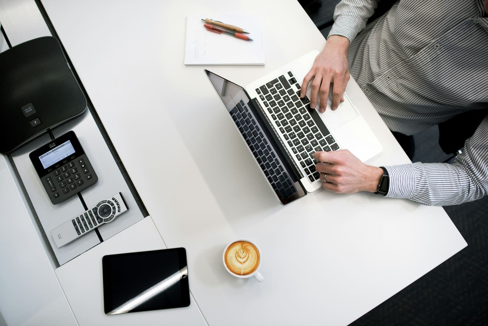Werkplek bij Finoptis met laptop, vergadertelefoon en koffie